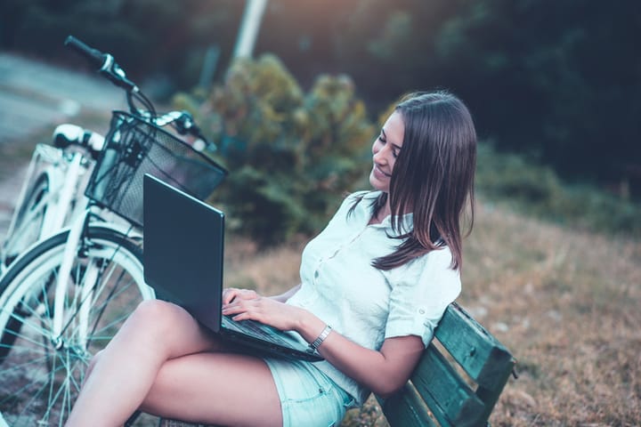 Young Smiling Woman how Sitting on Park Bench and Using her laptop after cycling.