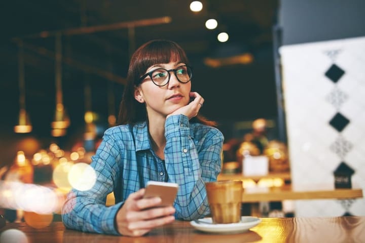 Shot of an attractive young woman looking thoughtful while texting on her cellphone in a cafe