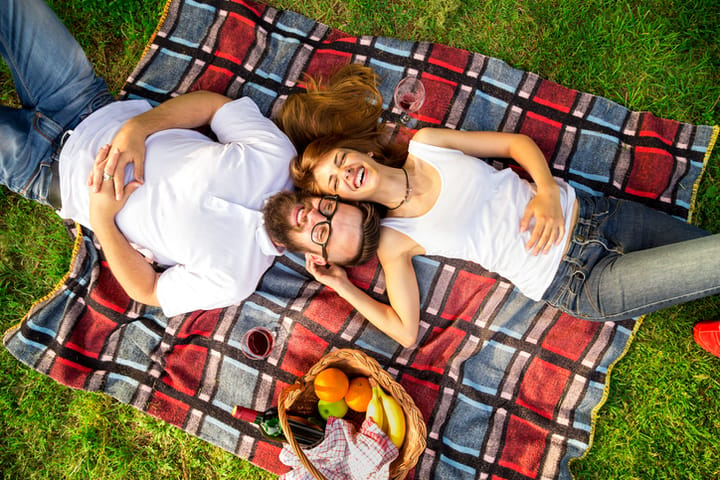 Top view of couple in love lying on a picnic blanket in the park with basket full of food and drinks placed next to them