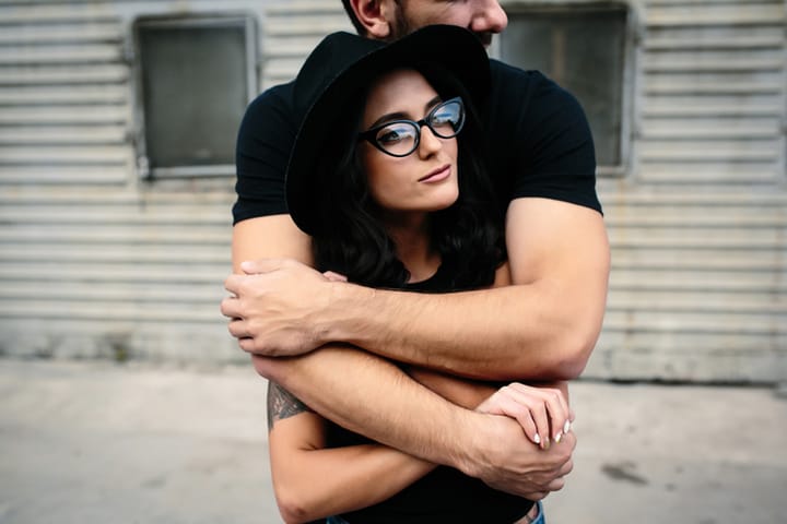 guy hugging his girlfriend from behind against a background of gray wall