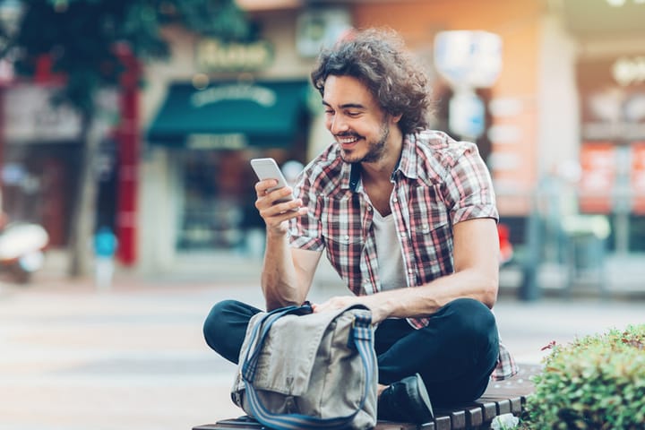 Young man with smart phone sitting on a bench