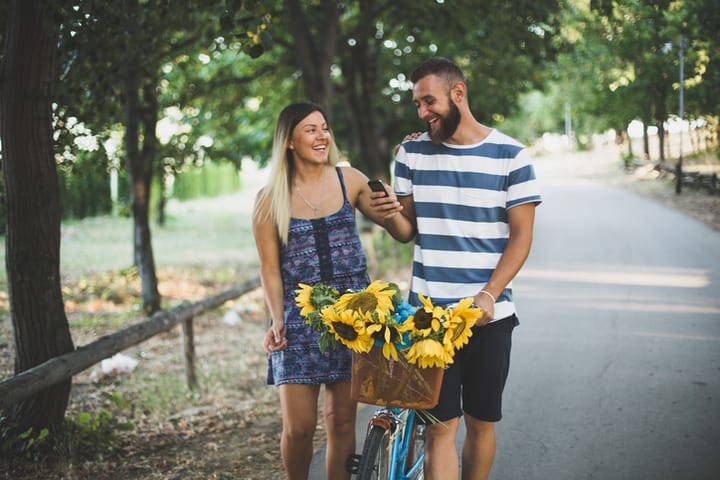 Beautiful stylish couple is using a smartphone and smiling while cycling in the park