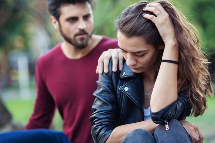Unhappy looking couple sitting in the park and discussing and feeling gloomy