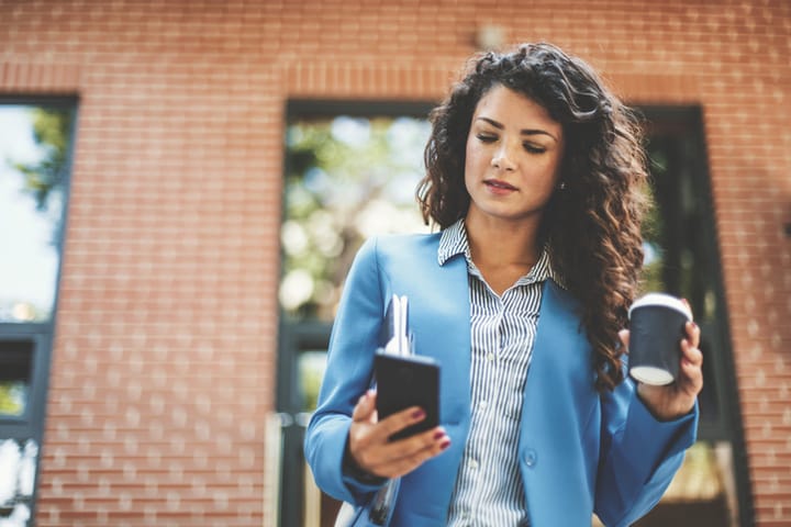 Woman with coffee to go with smart phone in front of cafe.