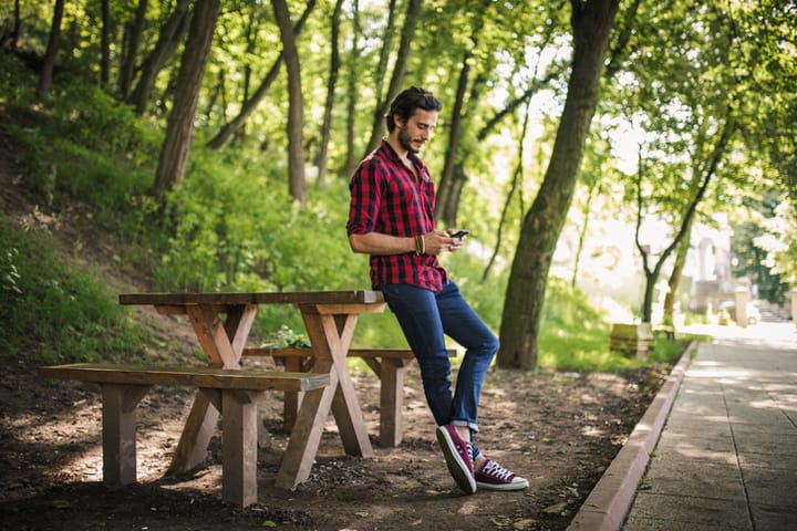Young man standing in the park and using a smart phone