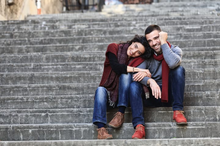 Young couple in love sitting on stairs. Girl lean on boy's shoulder.