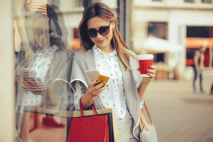 Cheerful woman is shopping in the city. She is using her smart phone.