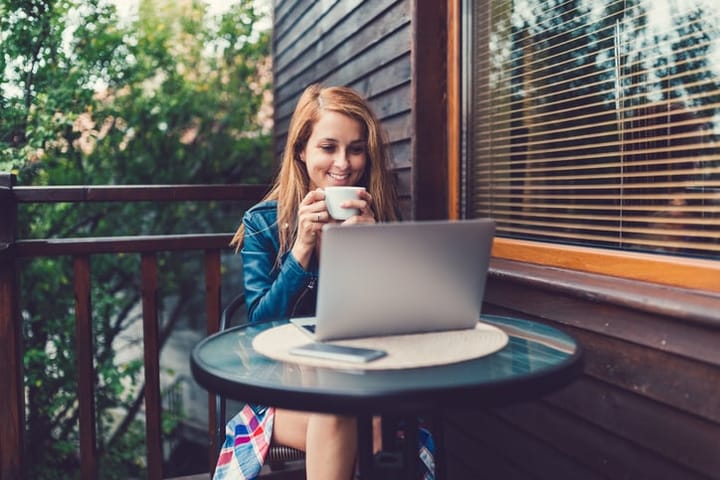 Young woman at holiday villa drinking coffee and using laptop