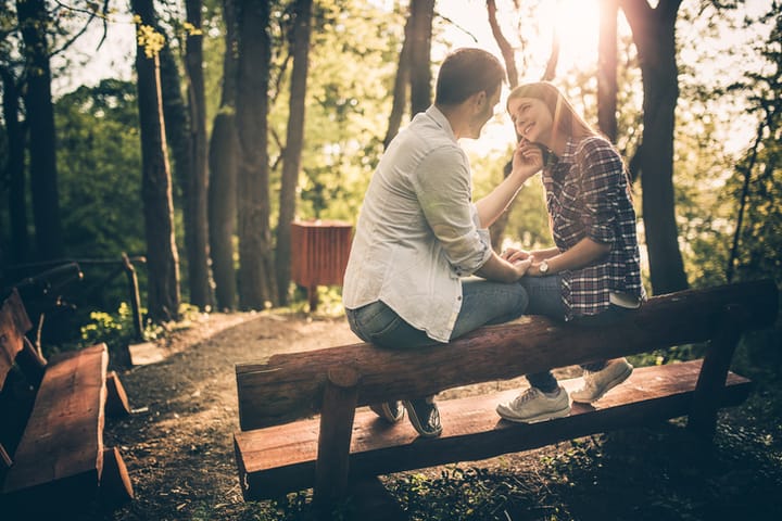 Young couple flirting while relaxing together on a bench in the forest.