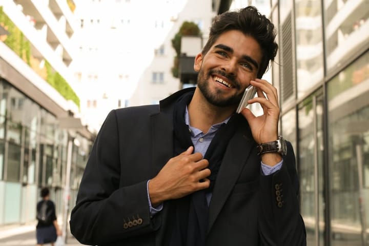 Businessman walking on city street and talking on smart phone.
