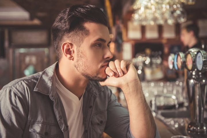 Handsome pensive guy is looking forward and thinking while leaning on the bar counter in pub