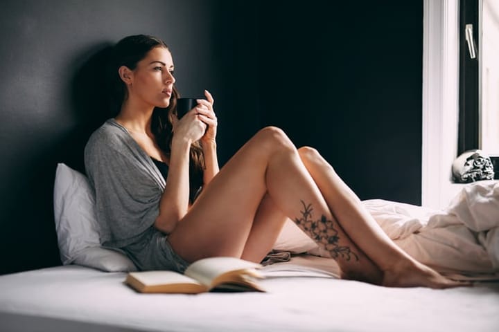 Thoughtful woman with her coffee mug on bed