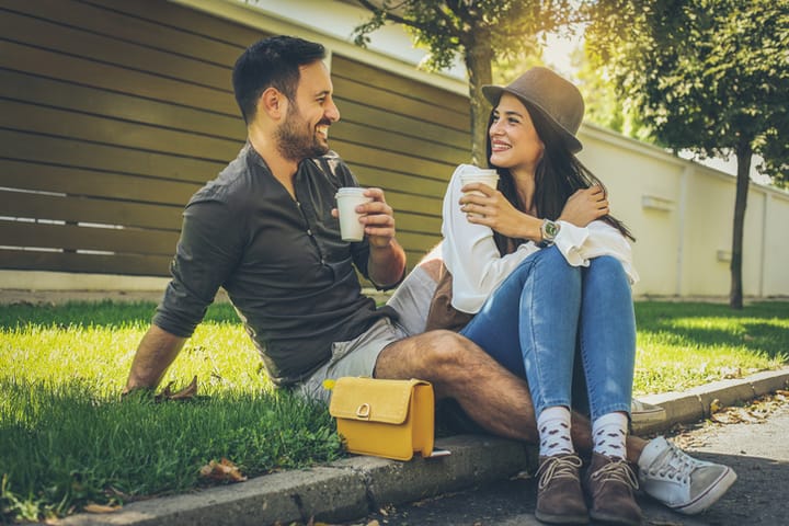 Happy young couple sitting in the park, drinking coffee. Spring season.