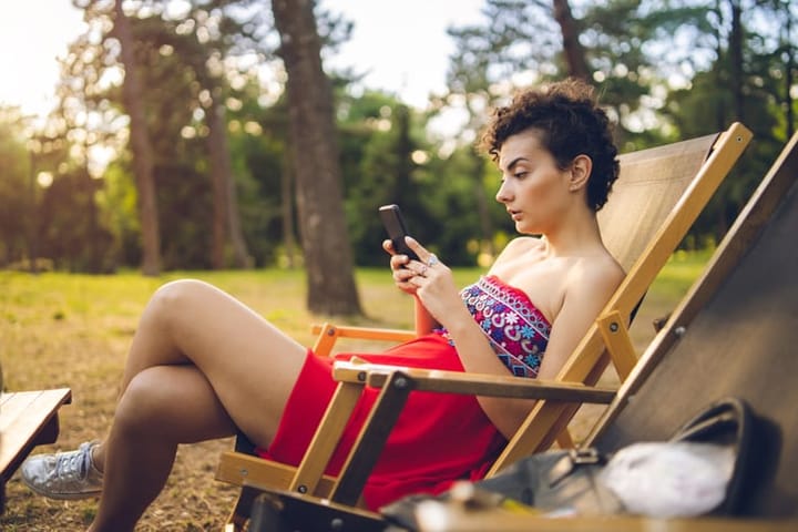 Caucasian cute girl surfing the net, sitting in chair in park.