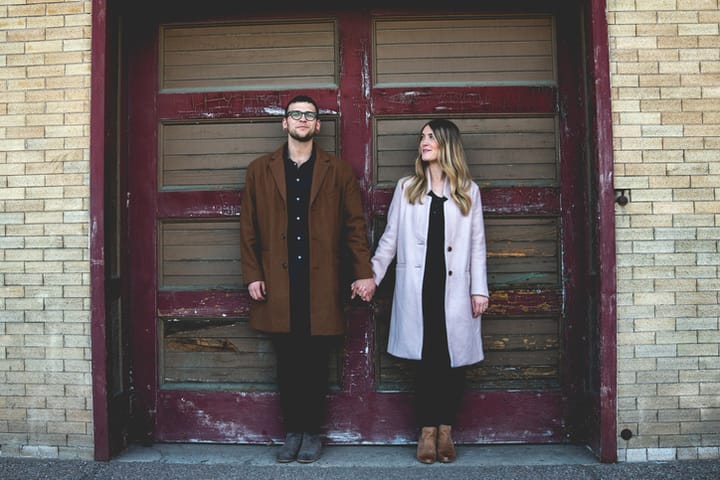 Cute Humorous Full Length Portrait of a Hipster Couple Posing in Front of an Old Garage Door