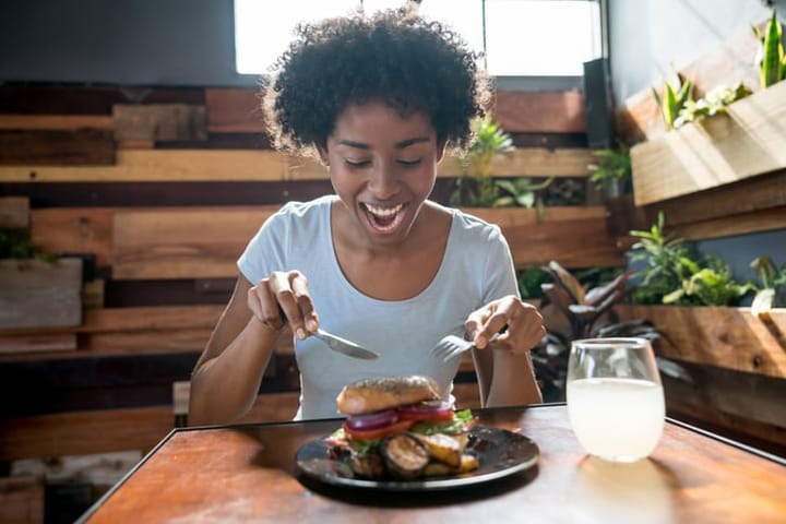 Beautiful african american woman eating a delicious bagel with vegetables