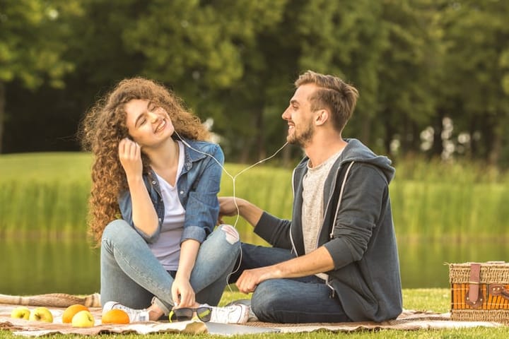 The happy man and woman sit with an earphones in the park