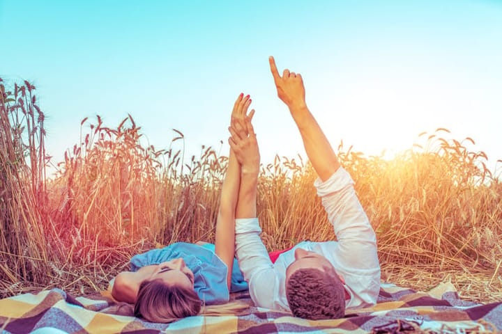 A young couple, man woman, in wheat field summer, lie on rug. Hand gestures indicate stars. Concept love, date, emotion, tenderness, warmth, care, romance. Happiness hugs lovers, young family.