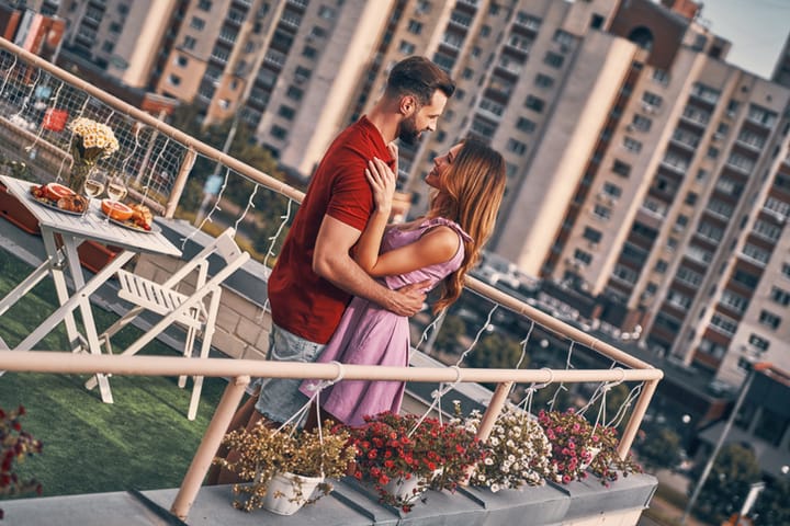 Loving young couple in casual clothing dancing and smiling while having romantic dinner on the rooftop patio outdoors