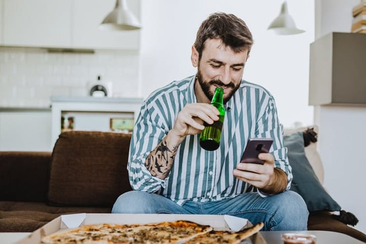 guy looking at his mobile while he's eating pizza