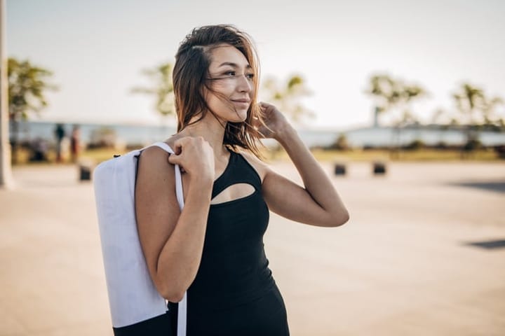 One woman, portrait of beautiful young woman holding a bag with exercise mat outdoors in city. She is going to exercise yoga.