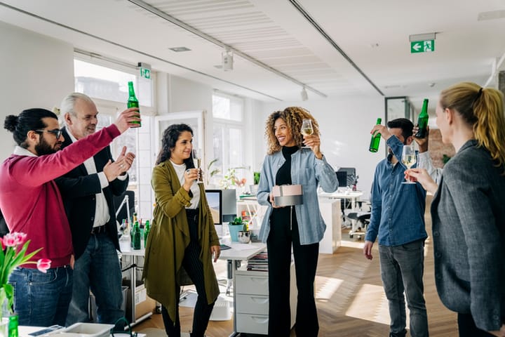 Business people having a party at office. Multi-ethnic business people raising beer bottles and wineglasses during a farewell party of a colleague at work.