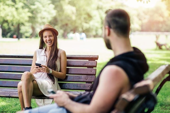 guy flirting with woman smiling on park bench