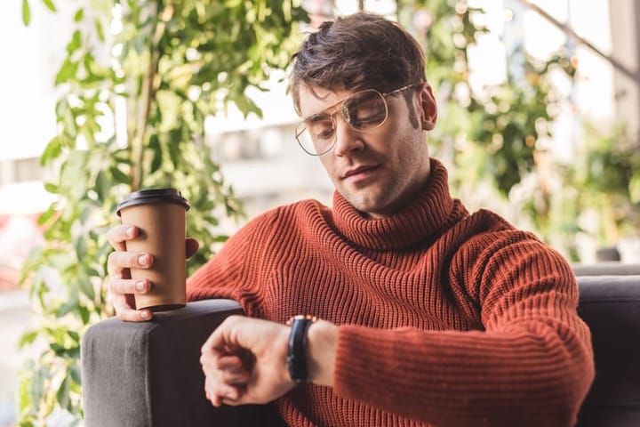 man in sweater holding coffee looking at watch
