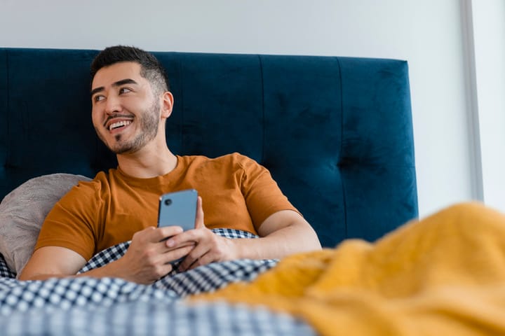 happy man texting in bed