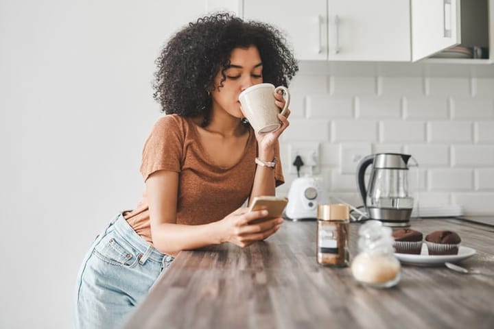 woman texting with coffee in kitchen