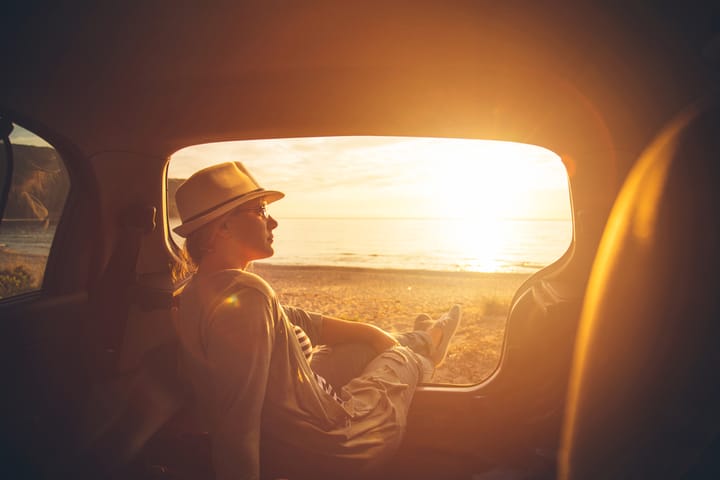 Young woman sitting in the trunk of a car on a beach in sunset