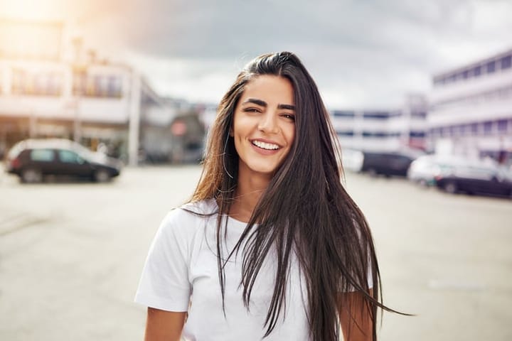 Smiling young woman in long brown hair and white short sleeve shirt walking in the middle of street