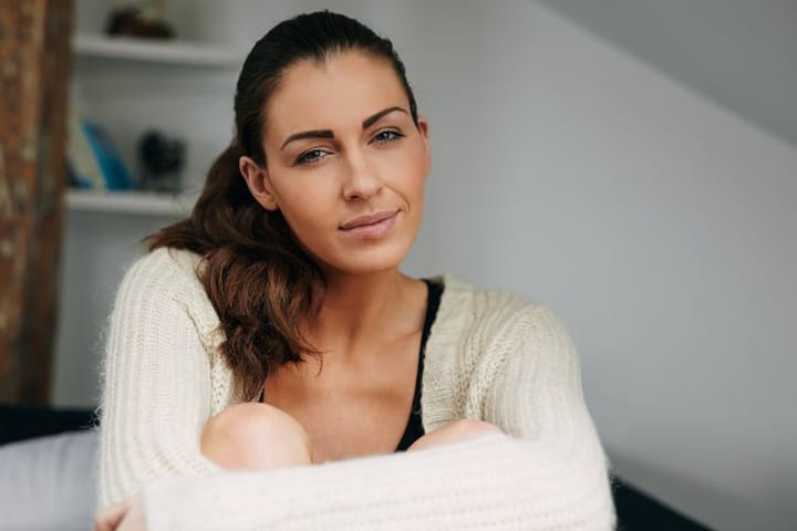 Portrait of beautiful young woman sitting at home looking at camera. Pretty relaxed woman indoors.