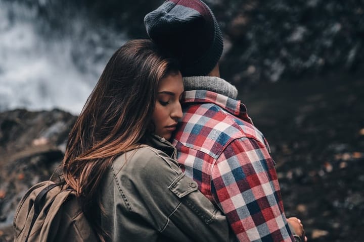 Young attractive woman embracing her boyfriend while standing near the waterfall
