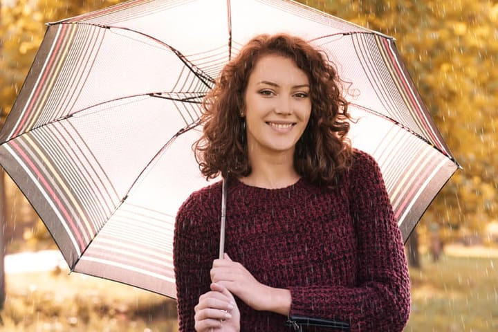 Young woman walking through park at autumn rainy day