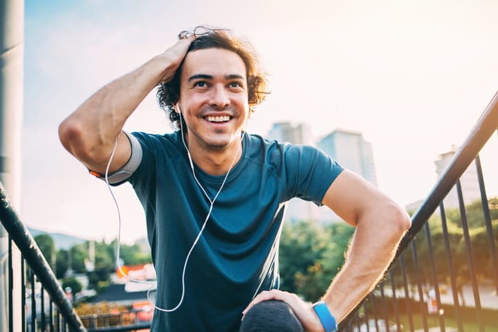 Young man in sports wear and with portable information devices making exercises at sunlight outdoors in the city