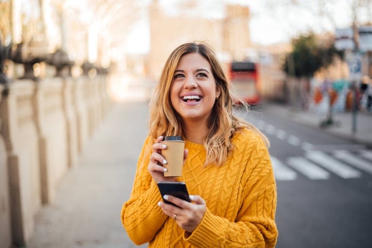 Young blonde smiling and holding phone and coffee in her hands