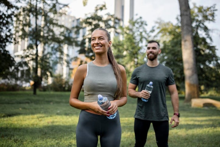 Portrait of happy fit people drinking water and running together outdoors. Couple sport healthy lifestyle