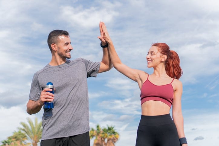 A young sporty couple smiling and high five to celebrate a succes workout in a sunny day. The sportman is holding a bottle of water. A man and a woman joying a helathy life and having a break