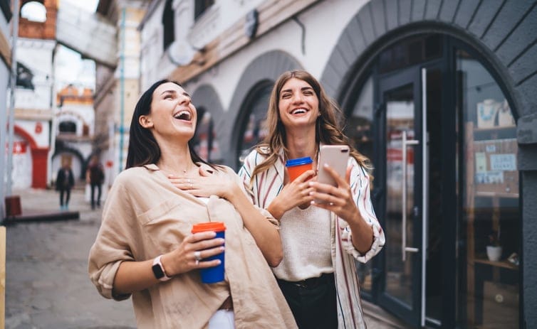 two smiling friends with coffee walking in city