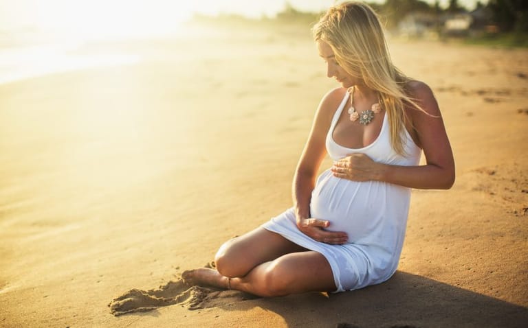 pregnant woman cradling bump on beach