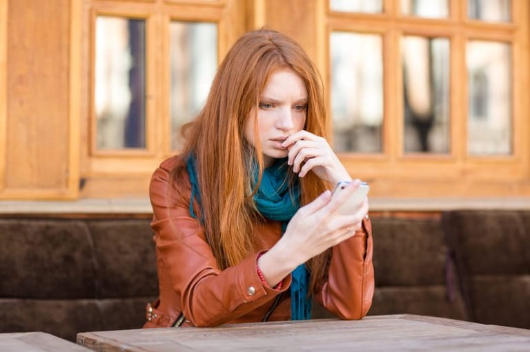 Upset woman staring at phone as if she's been ghosted