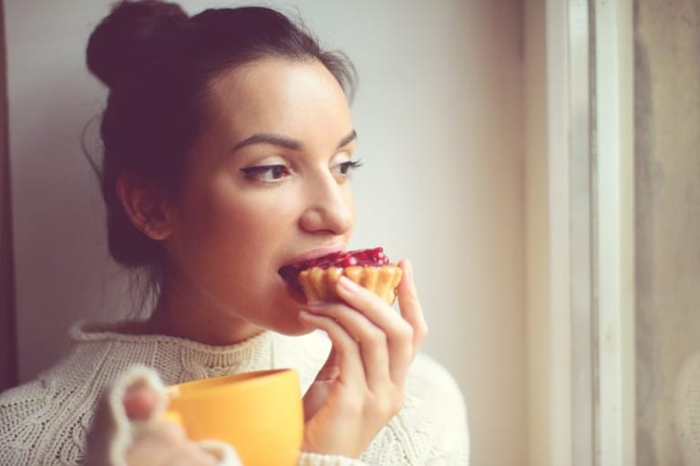 Girl eating tart drinking tea by window