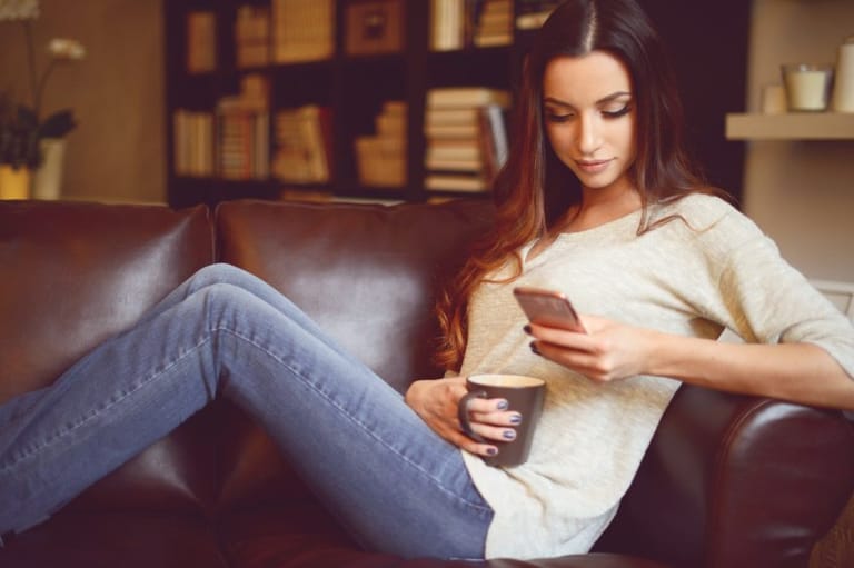 Long haired brunette sitting on sofa with phone