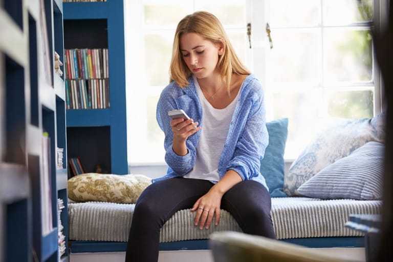 sad woman texting near bookshelves