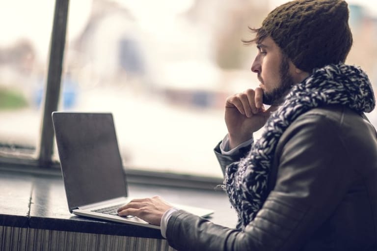 Profile view of pensive hipster man using laptop.