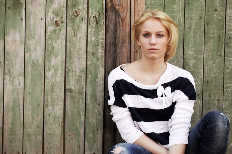 Young woman sits leaning against a wooden fence
