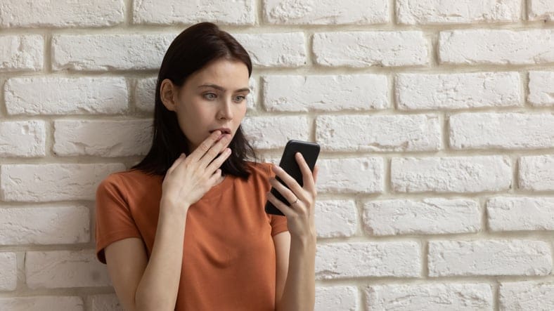 Shocked young woman looking at smartphone screen, getting scam spam social phishing message, reading unbelievable news