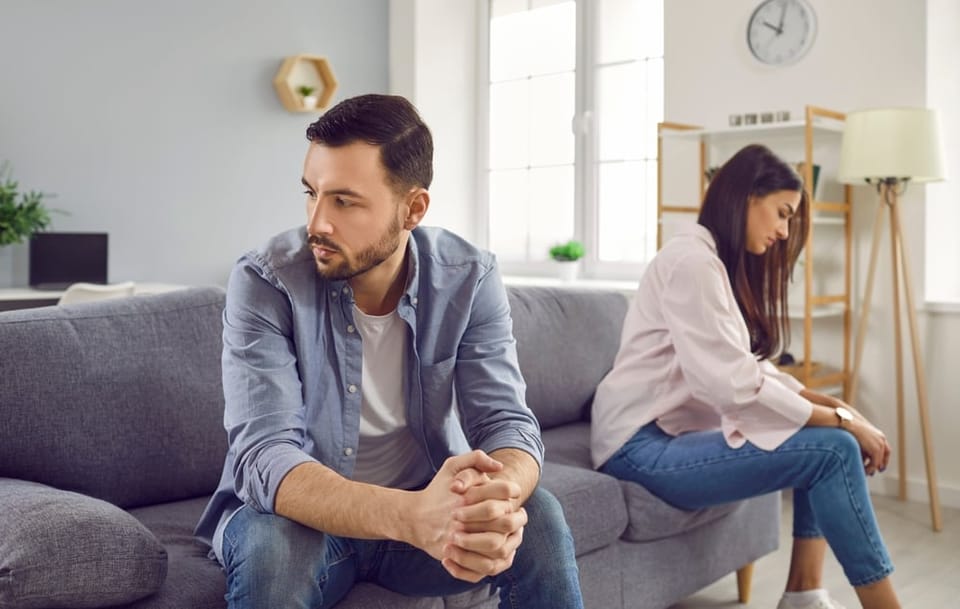Man and woman sitting on couch looking away from one another.