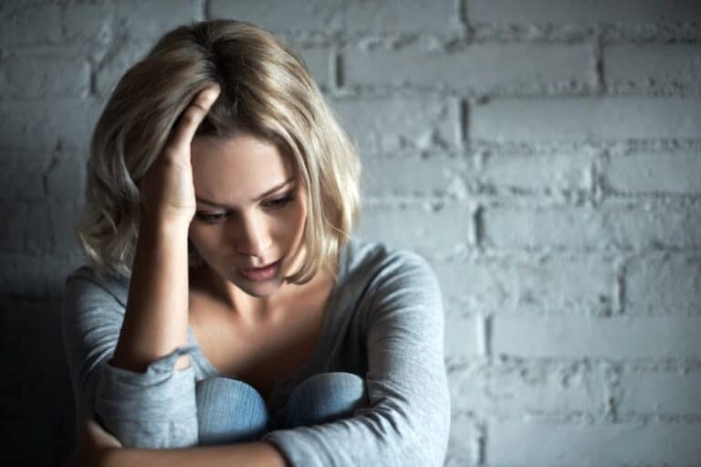Blonde woman sitting down while looking severely depressed